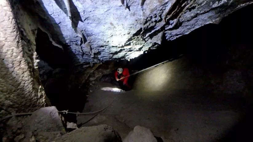 Persona descendiendo por una pendiente rocosa en el interior de una cavidad.