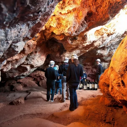 Personas con casco caminando por una galería iluminada con rocas rojizas.