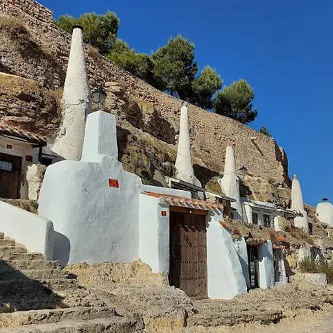 Vista lateral de casas cueva blancas alineadas bajo una muralla de piedra.