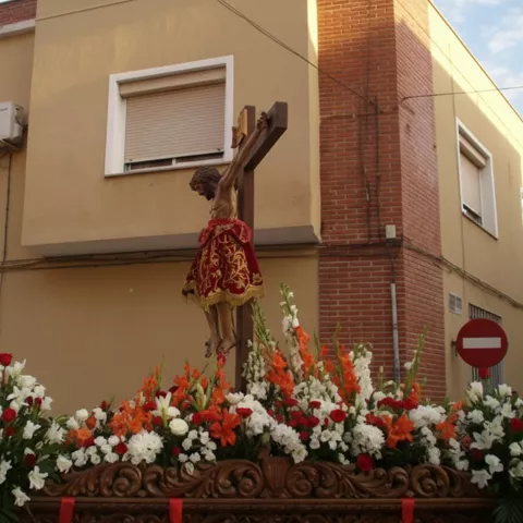 Paso procesional con crucifijo adornado con flores en una calle.
