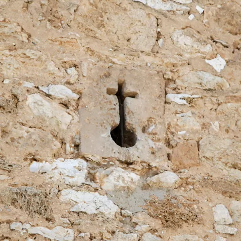 Detalle de muro de piedra con abertura en forma de cruz.