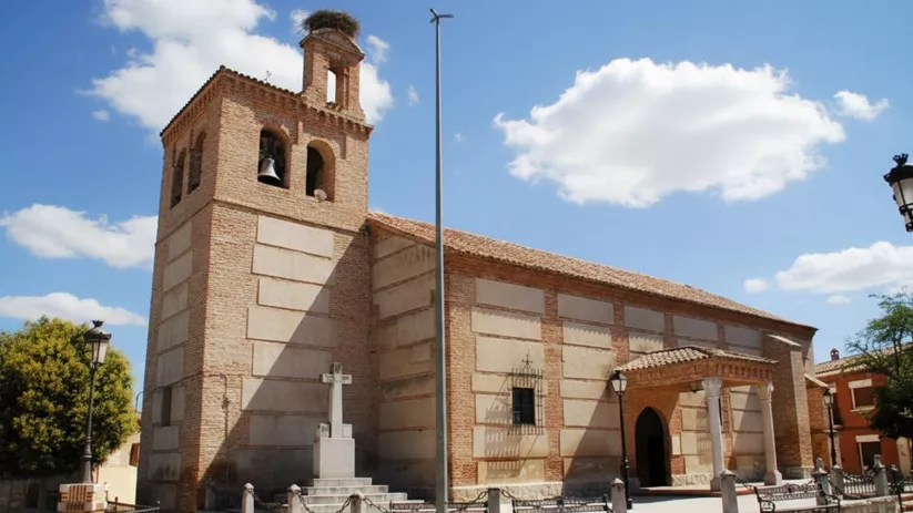 Iglesia de ladrillo visto, con espadaña, cruz de piedra y acceso porticado.