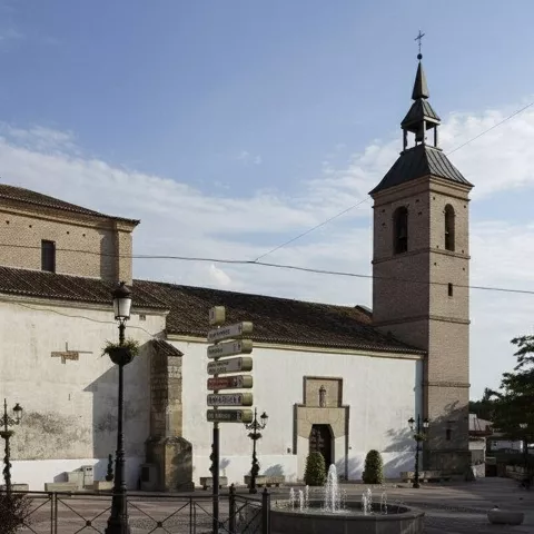 Iglesia de piedra con torre campanario junto a plaza urbana