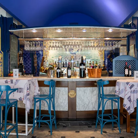 Barra curvada con taburetes azules y copas colgantes