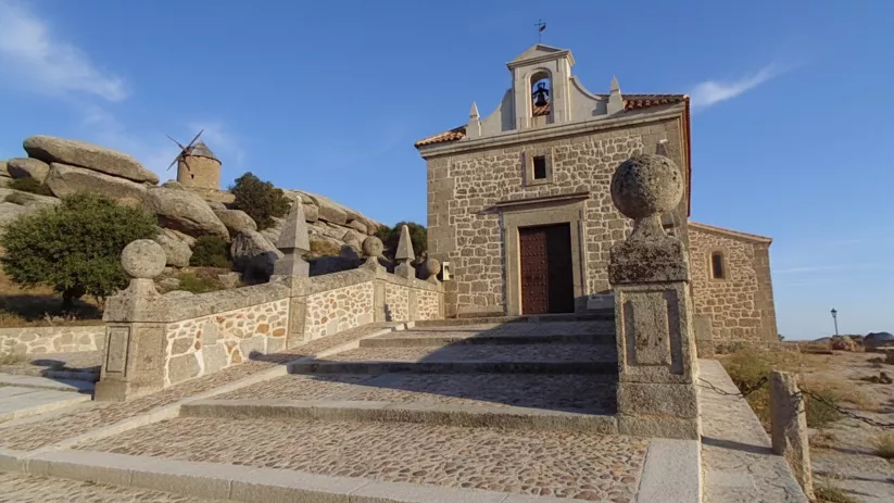 Fachada de ermita de piedra con molino al fondo