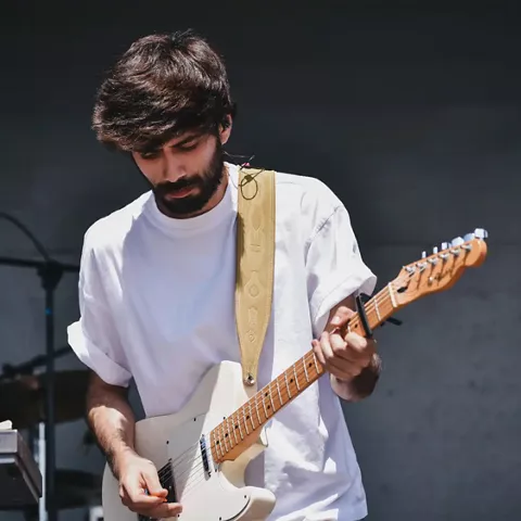 Guitarrista tocando en un escenario al aire libre durante un concierto.