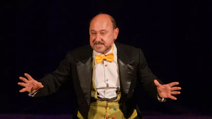 Actor con pajarita amarilla gesticula durante una actuación en escena