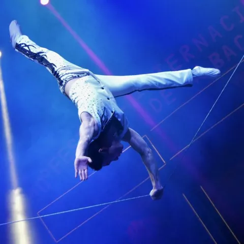 Acróbata suspendido realizando figura aérea bajo iluminación azul.