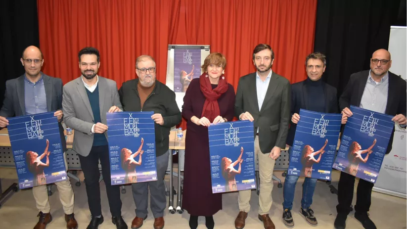 Grupo de personas presentando carteles en una sala con telón rojo.