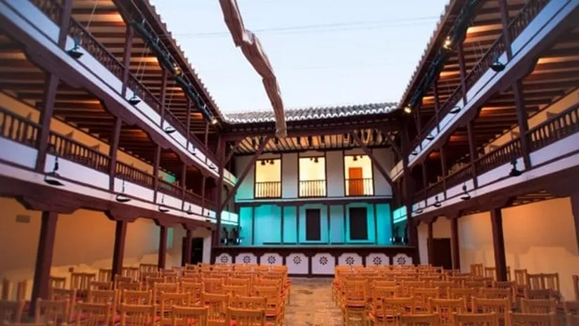 Patio escénico de arquitectura tradicional con estructura de madera, galerías superiores y filas de sillas.