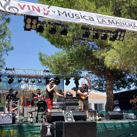 Banda actuando en un escenario decorado con carteles de vino y música durante el día.