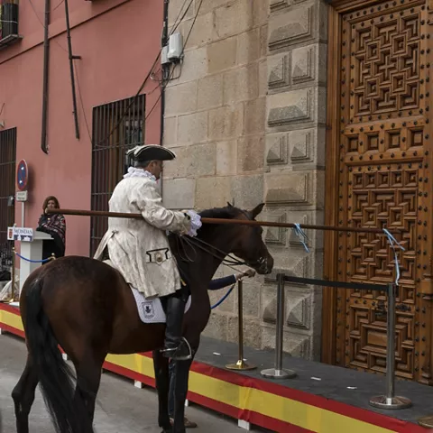 Escena ceremonial con jinete a caballo frente a un edificio histórico.