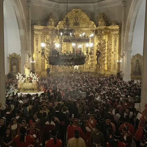Interior de iglesia llena de personas ante altar dorado.