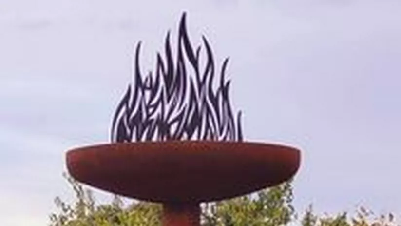 Escultura metálica de antorcha elevada sobre un pedestal.