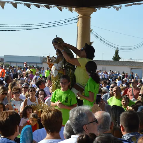 Personas rodeando una imagen religiosa bajo un pórtico durante un acto popular.
