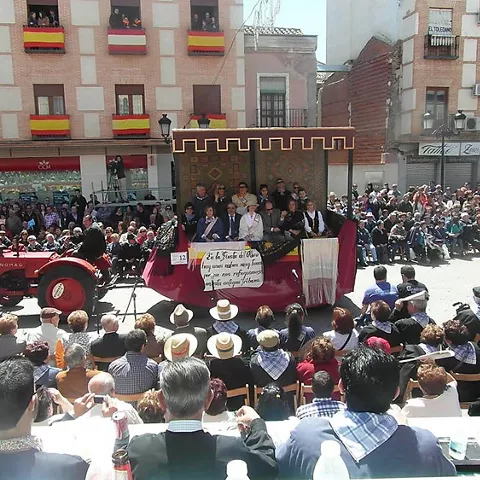 Carroza en desfile festivo por plaza llena de gente