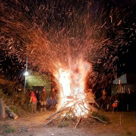 Hoguera nocturna con chispas y personas alrededor durante una celebración.