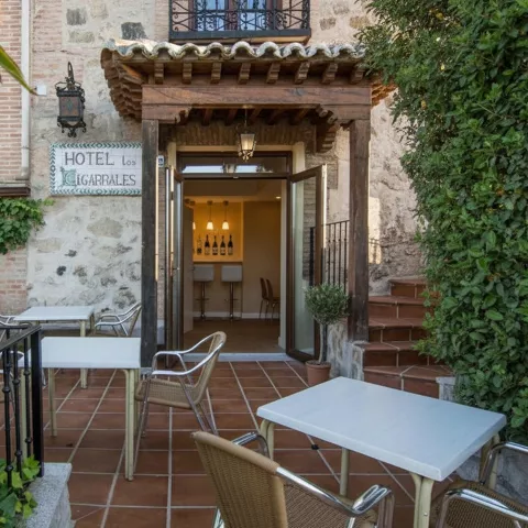 Entrada del hotel con mesas exteriores y vegetación alrededor.