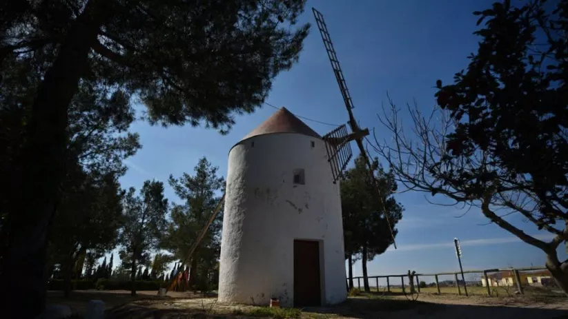 Molino de viento tradicional en Hoya Gonzalo rodeado de árboles y paisaje rural.