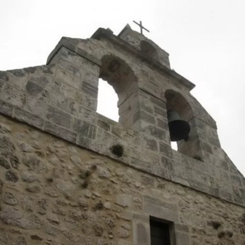 Espadaña de piedra con campana y cruz.