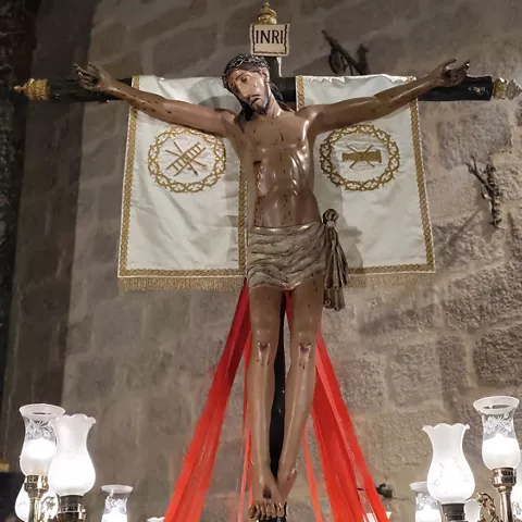 Escultura de un crucificado con paños y telas rojas en un interior religioso.