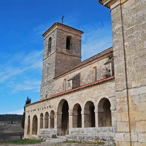 Iglesia de piedra con galería porticada y torre campanario.
