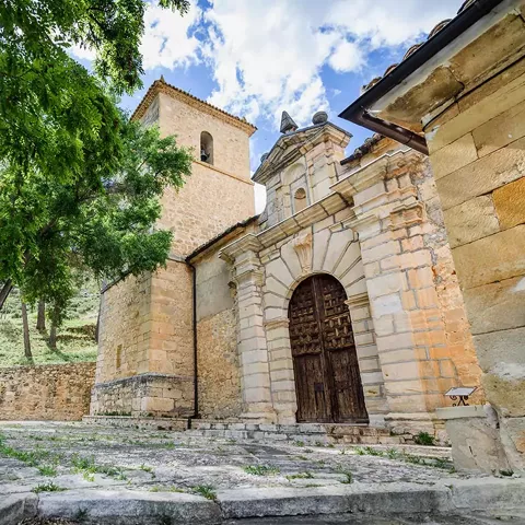 Iglesia de piedra con torre vista desde una plaza arbolada.