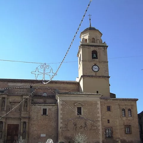 Torre de iglesia con reloj vista en ángulo, con cielo azul y guirnaldas de luces.