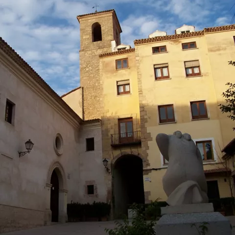 Plaza con iglesia, torre cuadrada y edificios tradicionales.