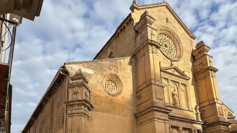 Fachada lateral de iglesia de piedra con portada barroca y rosetón.