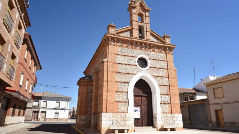 Vista lateral de iglesia pequeña con puerta de madera y óculo circular, rodeada de casas.
