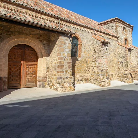 Fachada lateral de iglesia de piedra junto a una plaza abierta.