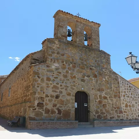 Iglesia de piedra con espadaña y campanas bajo cielo azul