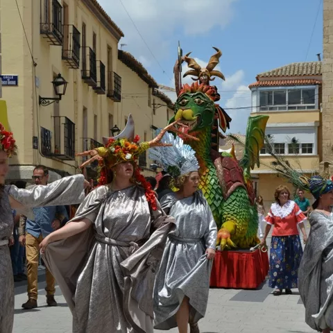 Desfile festivo con mujeres ataviadas y figura de dragón en una calle histórica.