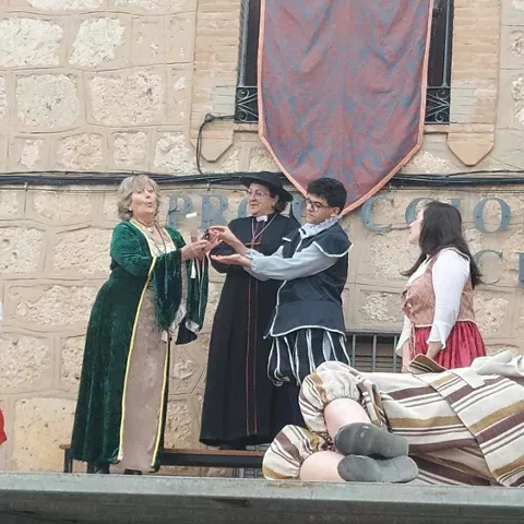 Grupo de actores con vestuario histórico saludando al público sobre un escenario al aire libre.
