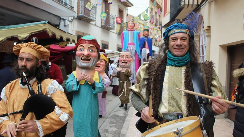 Pasacalles con músicos y figuras gigantes en una calle decorada