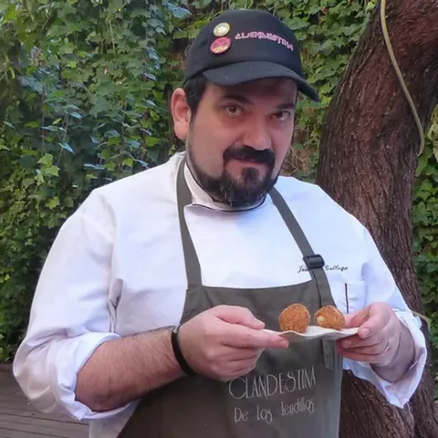 Cocinero con delantal sostiene dos croquetas en un patio con hiedra