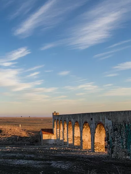 Restos de acueducto histórico en La Herrera junto a campos abiertos y árboles al atardecer.