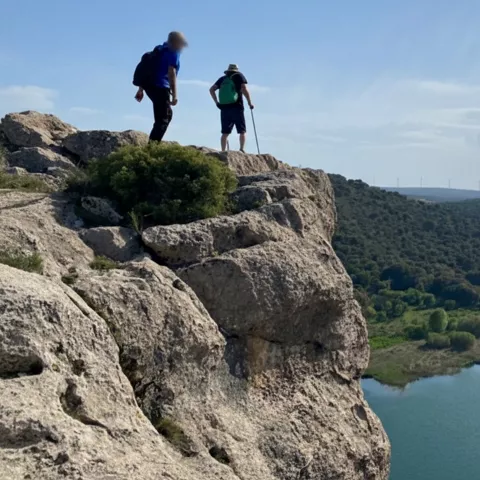 Dos senderistas en un acantilado con vista panorámica de un lago y valle.