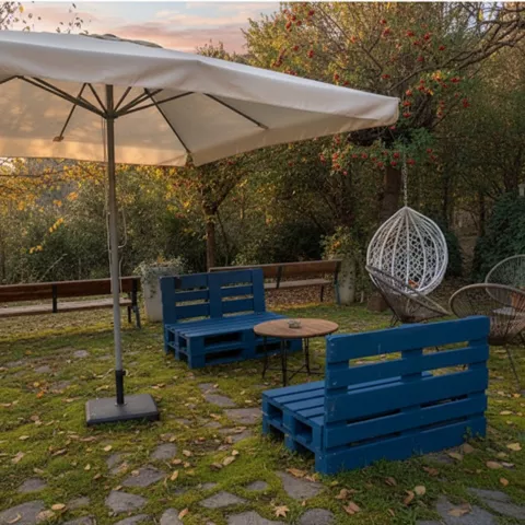 Zona ajardinada con sofás azules, sombrilla y sillas colgantes