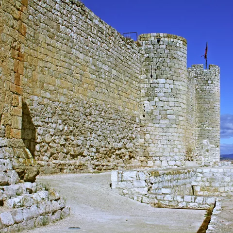 Lienzo de muralla con torre y horizonte rural.