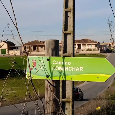 Señal verde junto a una carretera rural con casas al fondo
