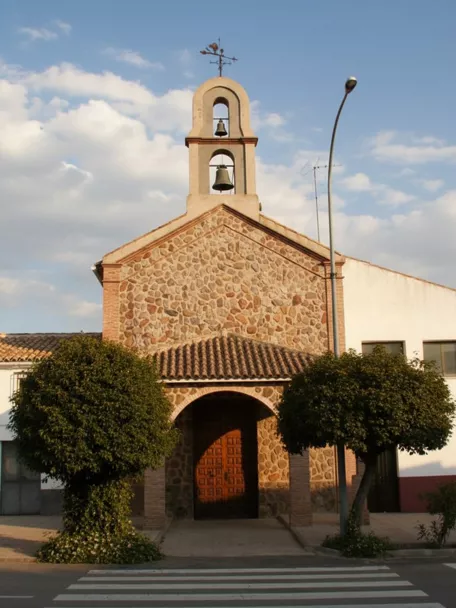 Iglesia parroquial de Los Cortijos con fachada de piedra y espadaña de doble campana.