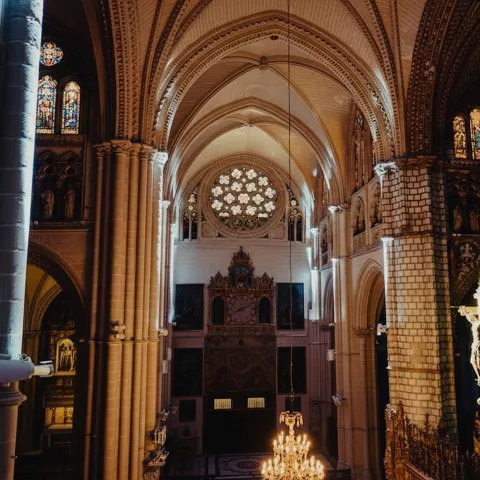 Interior de catedral con columnas altas, rosetón y crucifijo iluminado.