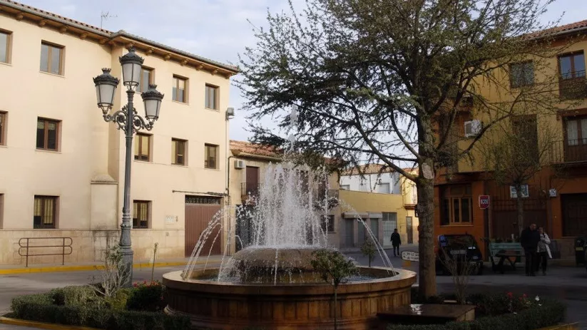 Fuente ornamental en una plaza de Madrigueras rodeada de edificios tradicionales y arbolado urbano.