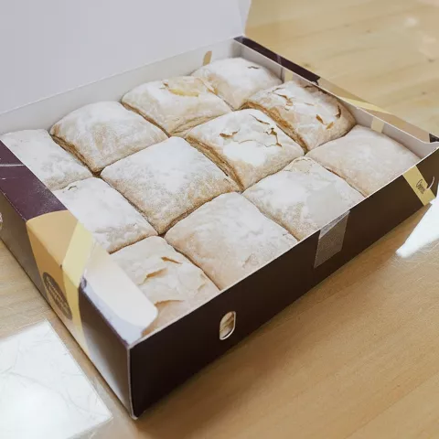 Caja abierta con pasteles cuadrados espolvoreados con azúcar glas sobre una mesa.