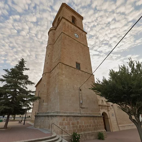 Torre campanario de la iglesia de Minaya en piedra clara bajo un cielo con nubes.