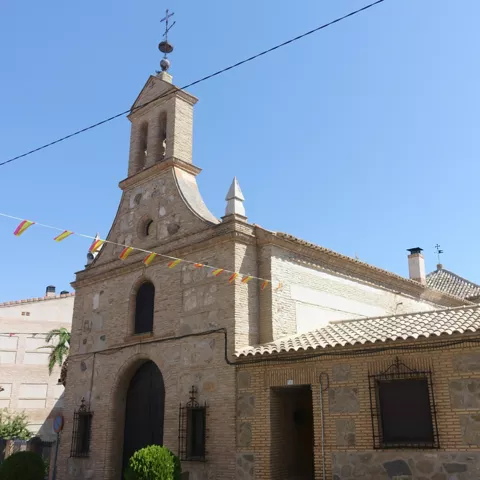 Ermita de piedra y ladrillo con espadaña y banderines en la calle