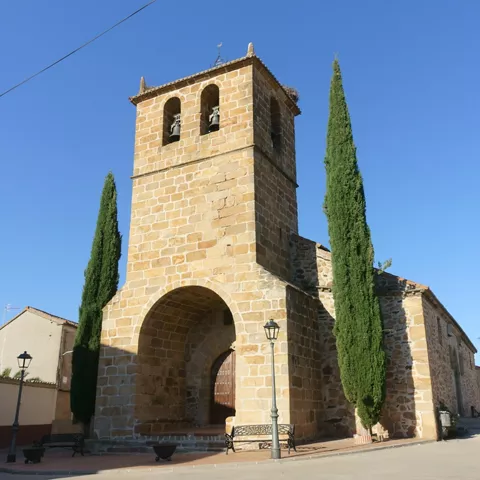 Iglesia de piedra con campanario y cipreses junto a la fachada