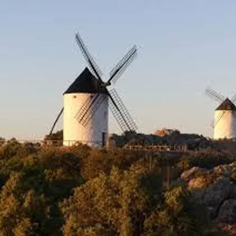 Dos molinos de viento sobre una cresta rocosa al atardecer, rodeados de matorral.